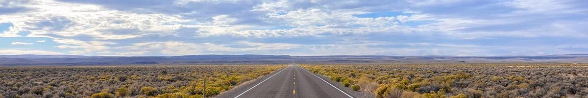 Open flat two lane highway going directly to the horizon with blue sky
